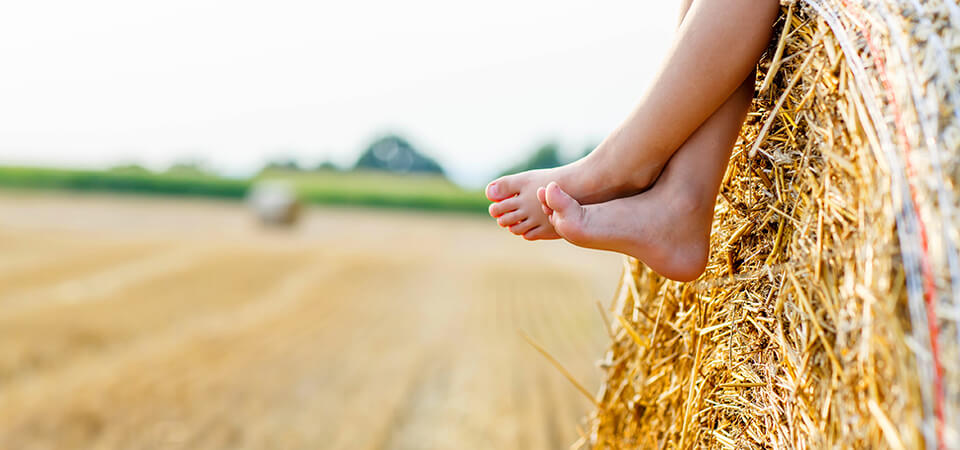 A barefoot child sits in harmony with nature on a hay bale. 