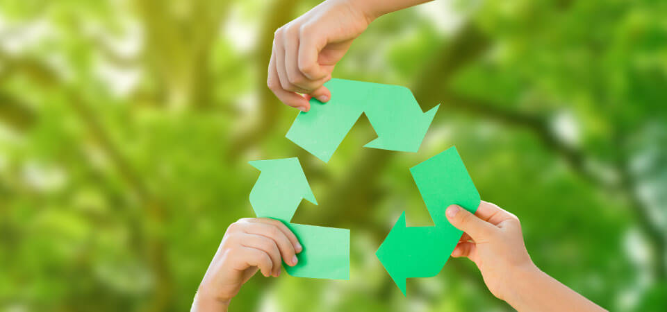 Drei Hände halten die drei Ecken des bekannten Recyclingsymbols aus Papier.