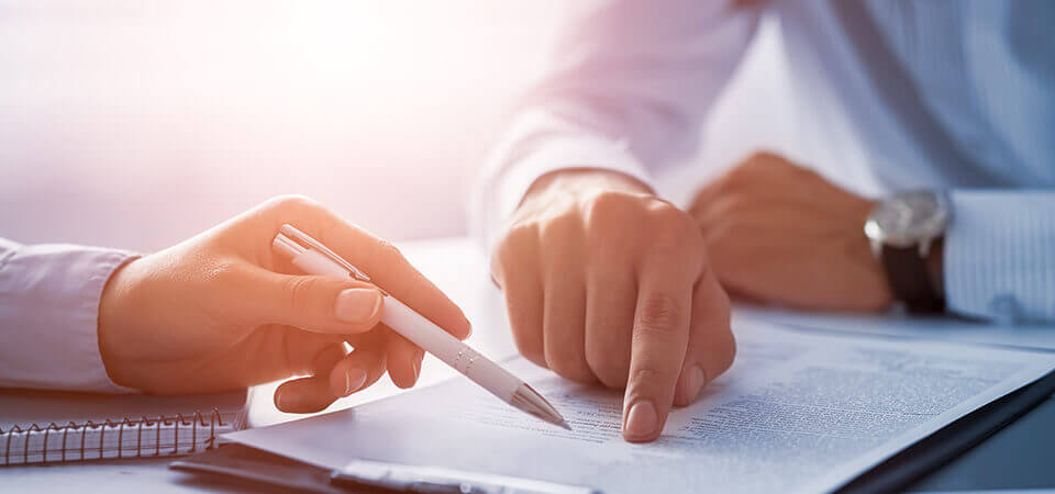 Hands and torsos of two men in business shirts pointing with finger and pen at papers lying on the table