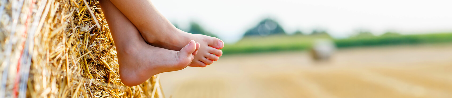 A barefoot child sits in harmony with nature on a hay bale.