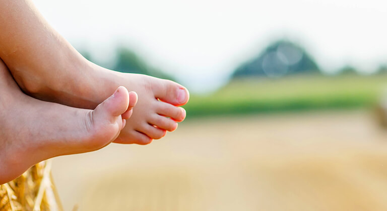 A barefoot child sits in harmony with nature on a hay bale.