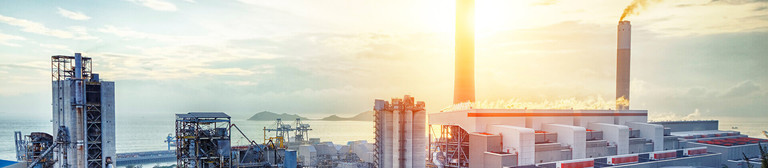 Industrial plant at sunrise; the sea in the background and trees in the foreground