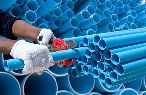 Unos tubos de plástico azules apilados y, en primer plano, las manos de un trabajador que corta los tubos con unas tenazas