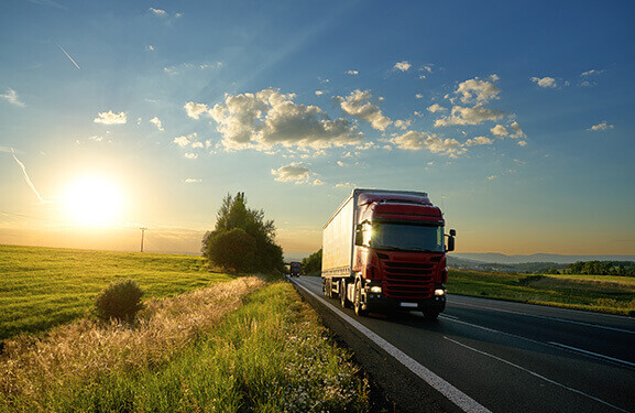 A lorry driving on a country road, surrounded by green landscape  