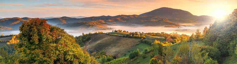 Un paisaje de Rumanía al amanecer con prados, bosques y montañas envueltas en niebla